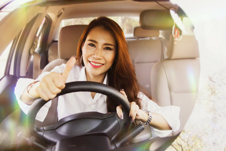 Beautiful asian woman wearing seatbelt spends her free time earning extra money by driving private taxi city public transport, thumbs up with confidence : Soft focusの写真素材