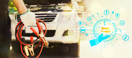 Male mechanic holds a car battery charger to provide emergency assistance to a car that won't start and fails during the trip : Closeup mechanic holding copper battery charger to aの写真素材