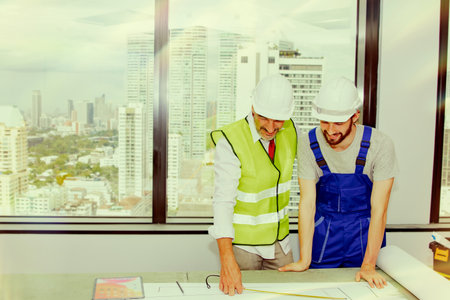 Senior architects and contractors for new office development project in a high rise building look at the blueprints on a wooden table together to discuss the success of the work.の写真素材