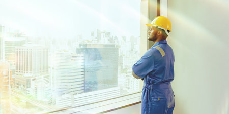 Asian male worker working at a construction site in a tall building in the city stands looking out of a glass window thinking positive and inspiring success.の写真素材