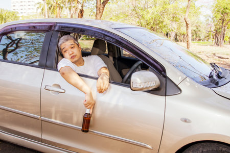 Young asian driver sits in a car holding a beer bottle, drinks alcohol from a drunken party and can't continue driving. Park on the side of the road for safety : Concept of not driの写真素材