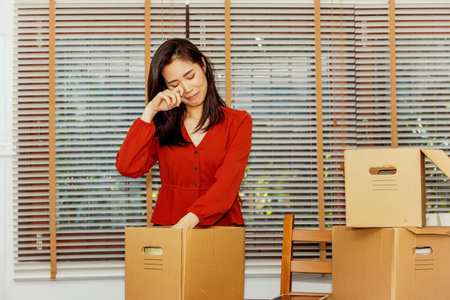 Asian female office worker working in a financial firm in economic hardship and epidemic packing room utensils in boxes crying in sorrow preparing to switch to a new job depressedの写真素材