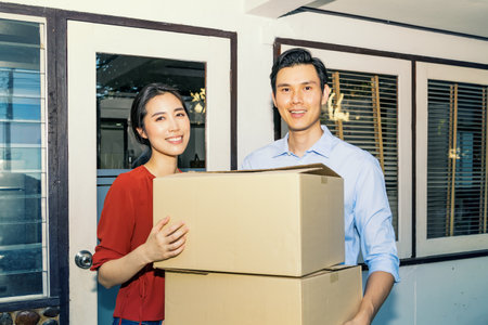 Happyness smiling asian family couple holding cardboard boxes stack to move to a new home with smiling faces : Moving the house to carry the necessary things to a new place conceptの写真素材