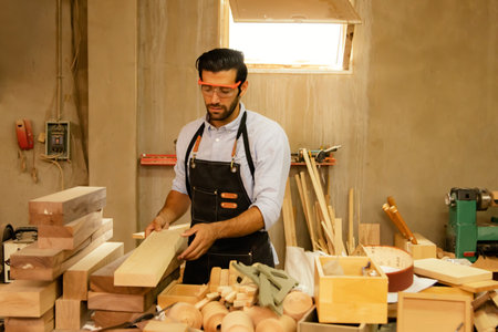 Caucasian male carpenter wearing safety glasses designing furniture on planks arrange the wooden boards on the table to prepare the furniture to keep things organized.の写真素材