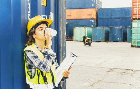 Female worker driving motorcycle works inspecting factory containers in the loading yard area....
