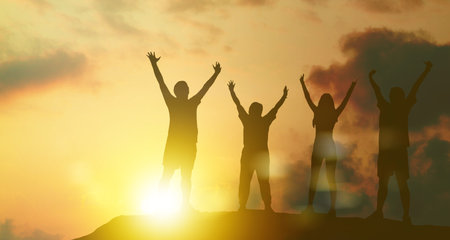 Silhouette of happy kids raising hands on sunset sky background.の写真素材