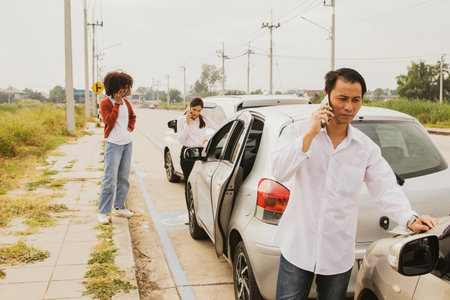 Man who was involved in a three vehicle collision standing stressed looking at the damage use phone to call the insurance company to clear and assess the initial damage to the otheの写真素材