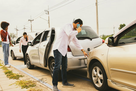 Man who was involved in a three vehicle collision standing stressed looking at the damage use phone to call the insurance company to clear and assess the initial damage to the otheの写真素材