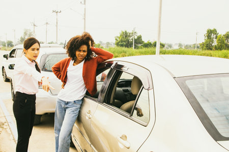 Asian woman driving after car crash on road upset pointing at brake marks wants to claim compensation from african american woman who stand reckless driving and she is at faultの写真素材