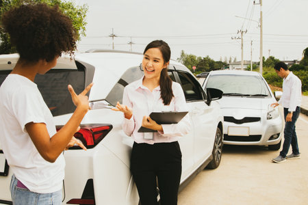 Car insurance company representative listens to information with smile about an accident from young woman driving car that crashed into the front to help assess the damage and payの写真素材