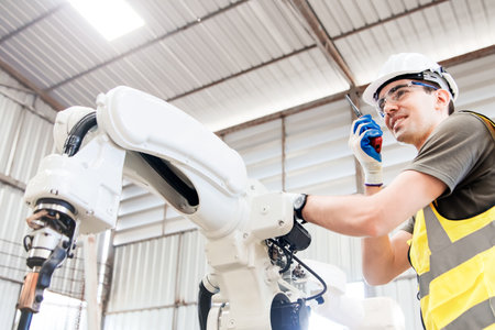 Male electronics engineer working in metal welding robot factory using radio to communicate with team while checking electrical system set, industrial robotic arm : Selected focusの写真素材
