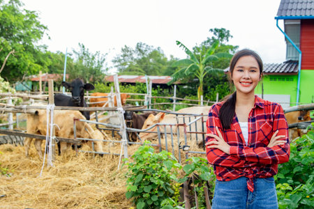 Portrait beautiful asian female farmer working as a livestock herder in the countryside raising cows in the farm at home : Female cowherd standing with hands crossed in front of haの写真素材