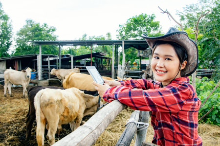 Portrait asian farmer veterinarian working the cattle area in a rural cowshed holding tablet taking care of the cows in a villager's farm looking at the camera and giving beautifulの写真素材