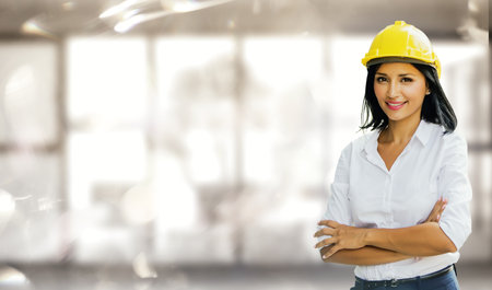 Portrait female architect engineer in safety helmet standing smart with crossed arms smiling confidently looking at camera with confidence standing in blurred modern office.の写真素材