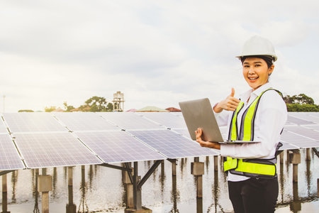 Professional asian female electrical engineer in helmet working in field working solar panel installation site in suburban area positive result thumbs up on tablet online to connecの写真素材