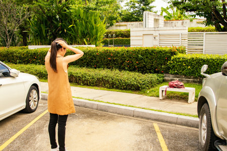 Concept lost car : Rear view Confused and sad Asian woman standing looking for her car parked in the parking lot lost, stolen, holding her head in confusion and sorrow stand helpleの写真素材