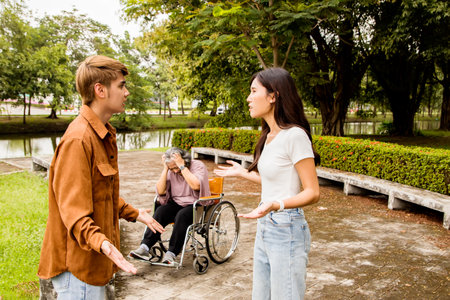 Disabled man in wheelchair talking with woman in park. Asian people