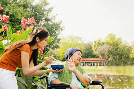 Daughter taking care health elderly mother who is sick with cancer sitting in wheelchair to eat soup to restore body and health but mother is bored of food doesn't want to eat blanの写真素材