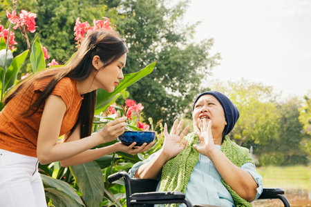 Daughter taking care health elderly mother who is sick with cancer sitting in wheelchair to eat soup to restore body and health but mother is bored of food doesn't want to eat blanの写真素材