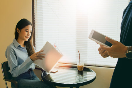Beautiful Asian female customer having lunch looking through food and drink menu ordering, male...