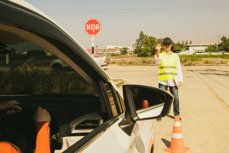 Young asian woman preparing for a driving test : Male driver in charge of the driving test gives hand signal to the young woman to drive safely during the road transport driving liの写真素材