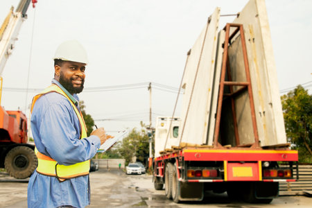 African American construction inspector foreman worker notes on clipboard, inspects concrete walls, prefabricated house construction on construction site delivery truck, checks befの写真素材