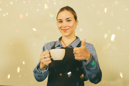 Coffee and food service business concept : Beautiful spanish barista holding cup of coffee smiling and looking at camera showing thumb up.の写真素材