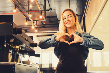 Portrait beautiful female hispanic barista who serves the work in front of the counter sends hearts to you and lovely smile customers who come to use the service with sinceerity.の写真素材