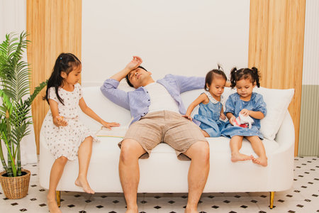 Father took care of his daughter until he was exhausted : Single father with three daughters in the living room finds time to take a nap exhausted by his mischievous daughter playiの写真素材