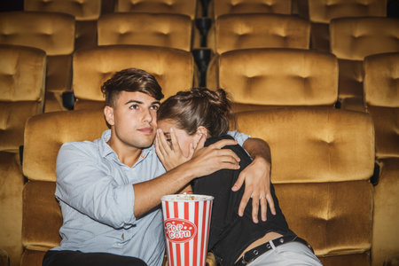 Caucasian couple watching scary horror movie in a multiplex movie theater, shocking their girlfriends, dare not look, can only hug and protect them safely in a warm romantic embracの写真素材