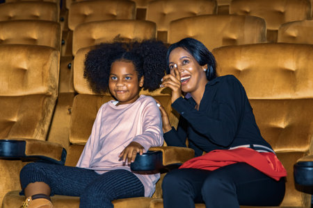African american mother and daughter two people sit and watch entertainment movie in cinema watching daughter's favorite movie laughing and smiling having fun relax family love onの写真素材