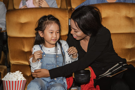 little girl asian crying in the cinema after watching scary movie kind african american woman gave her hug to calm her fears and stop crying, trying to calm her down.の写真素材