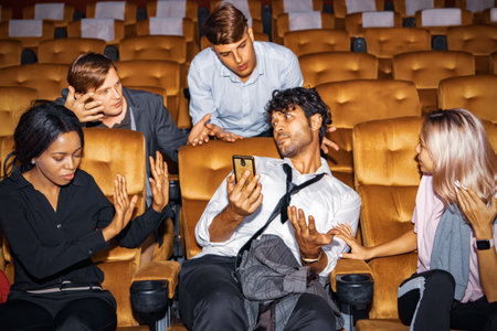 Concept Etiquette in the cinema Do not talk on the phone to disturb others : Man who is talking on the phone among moviegoers is annoying those around him who are upset for bad behの写真素材