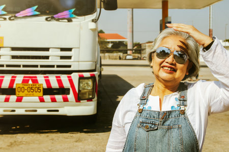 Asian senior female worker covering the sunlight working fuel truck driver in a warehouse or gas station : Elderly woman worker with experience and ability to transport NGV and oilの写真素材