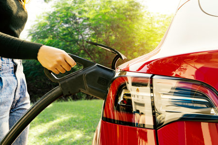 Hand of young woman driving EV car or Electric car holding DC power plug into her red electric vehicle battery socket : Clean energy vehicles, alternative energy that are becomingの写真素材