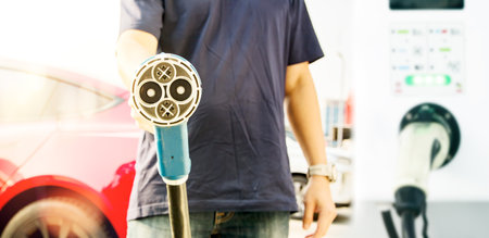 Electric car plugged : Man driving red EV or electric car standing in front of the power supply of the control cabinet holding power socket. The DC power supply head adds power toの写真素材