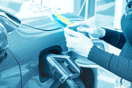Young female hand driving EV car checking and running application to connect to electric power supply system to charge DC power to vehicle and pay for electricity usage at public gの写真素材