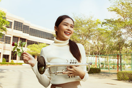 International music teacher in school : Portrait beautiful healthy asian teacher holding bright red rose and trumpet in front of school building Show flowers with friendly smiles tの写真素材