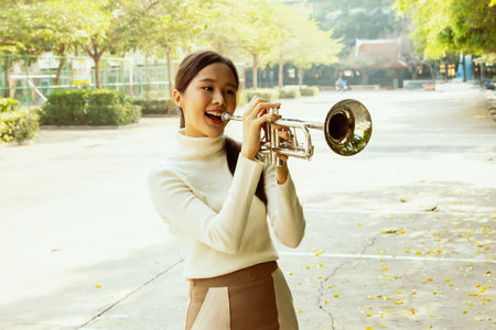 Beautiful asian teacher using sound power standing blowing instrument playing trumpet beautiful jazz instrument smiling good mood in front of school building : Jazz music improvesの写真素材