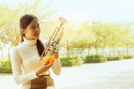 Pretty asian teacher uses cloth to clean the trumpet of the instrument to make it clean shiny and free from dust and dirt in preparation for teaching the students of the internatioの写真素材