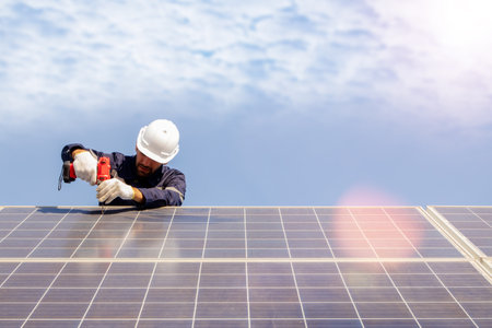 Male technician installing solar panel using electric drill securing solar system installation structure outdoors working outdoors : concept of renewable energy constructionの写真素材