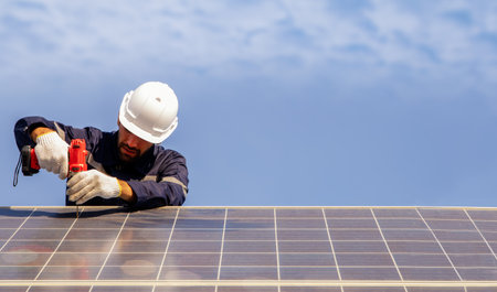 Male technician installing solar panel using electric drill securing solar system installation structure outdoors working outdoors : concept of renewable energy constructionの写真素材