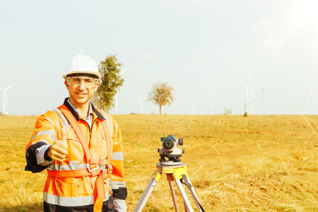 Clever explorer male architect thumbs up with surveyor's telescope to explore the wind farm area to plan road construction with professional tools using the high and low level cameの写真素材