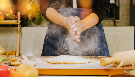 Hands of a female chef preparing a pizza, the process of mixing the wheat flour to make it evenly spread on the pizza dough on a rolling pin table to soften it in the kitchen at aの写真素材
