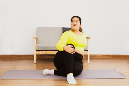 Asian fat woman wearing yellow sportswear at home light fitness exercises sit on a yoga mat flex your knees Keep your balance and relax take time to take care of your health : Healの写真素材