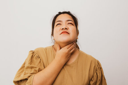 Asian obese woman having abnormal symptoms holding her neck with her hands because of pain feeling that there is a lump stuck in her throat which is a dangerous sign of oral cancerの写真素材