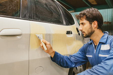 Skilled male car mechanic uses trowel and putty to reinforce smooth, clean surface as a paint job in preparation for smoothing and before repainting : Auto mechanic car accident inの写真素材