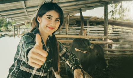 Thai female farmer : Portrait smiling happy farmer young asian proud worker working in agriculture caring for the beef farm caring for the cows in the stall with great thumbs up loの写真素材