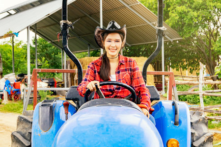 Portrait beautiful asian woman in a cowboy hat safely driving large tractor and smiling cheerfully looking at the camera : Very happy female farmer working in the field of livestocの写真素材