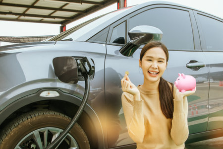 Portrait young asian woman driving an EV electric car In the process of charging smile good mood shows coin and piggy bank : Concept of using electric cars to save costs and have sの写真素材